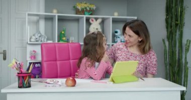 Uzaktan öğrenme çevrimiçi eğitim. Dijital tabletli liseli kız okul ödevi yapıyor. Annem evde kızıyla ödev yapıyor..