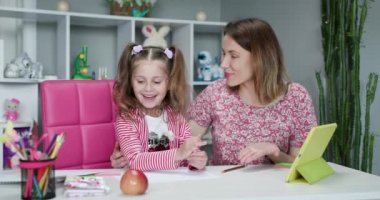 Anne ve kızı internette ödev yapıyor. Uzaktan öğrenme çevrimiçi eğitim. Dijital tablet dizüstü bilgisayarı olan ve okul ödevi yapan kız öğrenci. Annem evde kızıyla ödev yapıyor..
