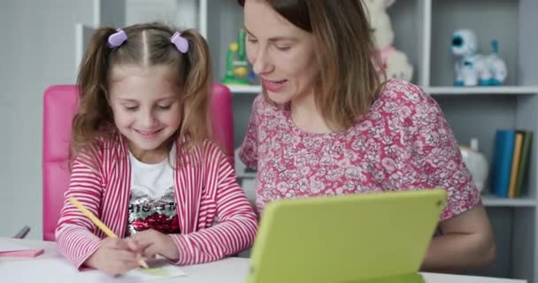 Tablet de uso infantil para educação, estudo on-line, estudo em casa. A rapariga tem trabalhos de casa no ensino à distância. Conceito de estilo de vida para a quarentena familiar covid-19. Mãe ajuda filha — Vídeo de Stock