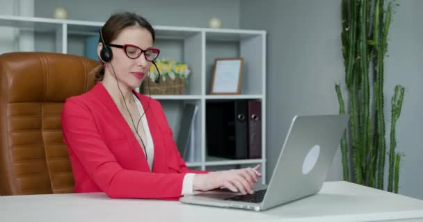 Ευτυχής γυναίκα φορούν ακουστικά επικοινωνίας με κλήση συνέδριο μιλούν κοιτάζοντας κάμερα στο γραφείο στο σπίτι. Συνέντευξη εργασίας συνομιλίας βίντεο ή μάθημα εξ αποστάσεως γλώσσας με την έννοια του online δασκάλου — Αρχείο Βίντεο