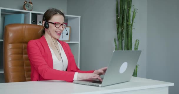 距離教育の概念。若い女性は、オンライン教師の勉強とノートパソコンの話を呼び出しヘッドセット会議を身に着けています,自宅から働く. — ストック動画