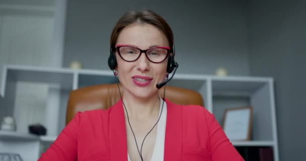 Gelukkig jonge vrouw dragen headset communiceren door middel van conference call spreken kijken naar de computer op kantoor. Video chat job interview of op afstand taalcursus met online leraar concept — Stockvideo