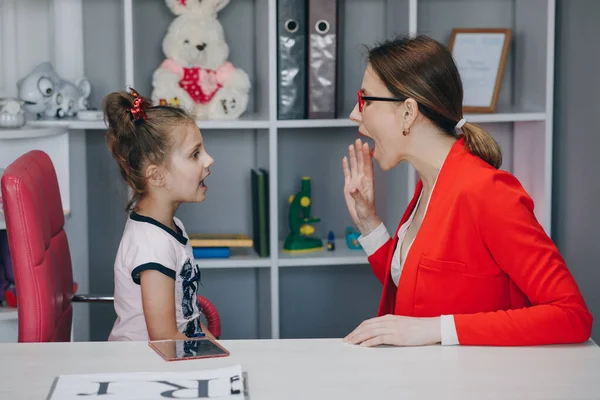 Linda niña en la oficina de fonoaudiólogos. Pequeño niño practicando la articulación con el terapeuta en una lección privada en casa — Foto de Stock