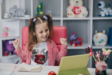 Kişisel izolasyon ve online eğitim. Uzaktan öğrenme, okul çevrimiçi. Kitaba bakıp gülümseyen bir anaokulu kızının portresi.