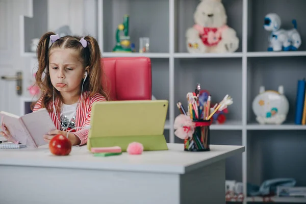 Küçük kız video çekiyor, özel ders veriyor, notlar yazıyor, ders veriyor. Anaokulundaki kız çevrimiçi ders izliyor ve evden ders çalışıyor. Bilgisayar ekranına bakarken not alan kız çocuğu. — Stok fotoğraf