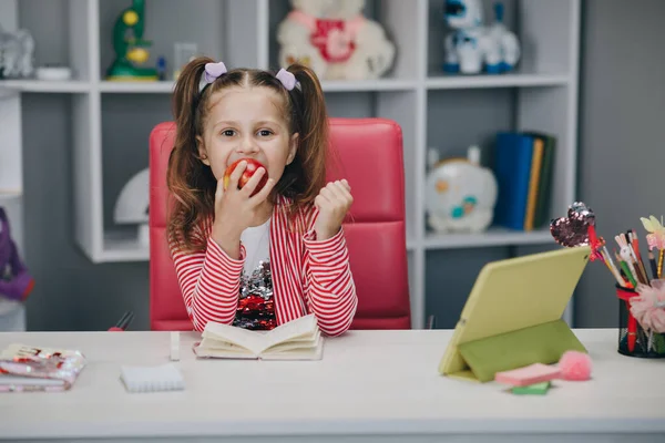 Elma yiyen küçük bir kızın portresi. İnternetten ders alırken elma yiyen tatlı küçük kız.. — Stok fotoğraf