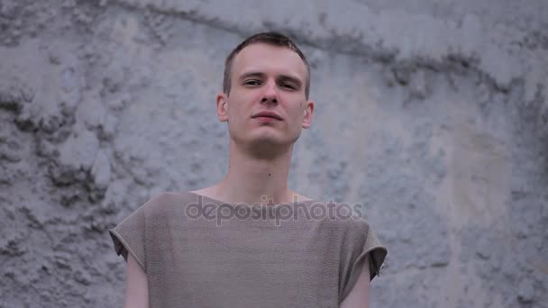 Молодий чоловік у сірий футболку стоїть на тлі стіна сірий камінь — стокове відео