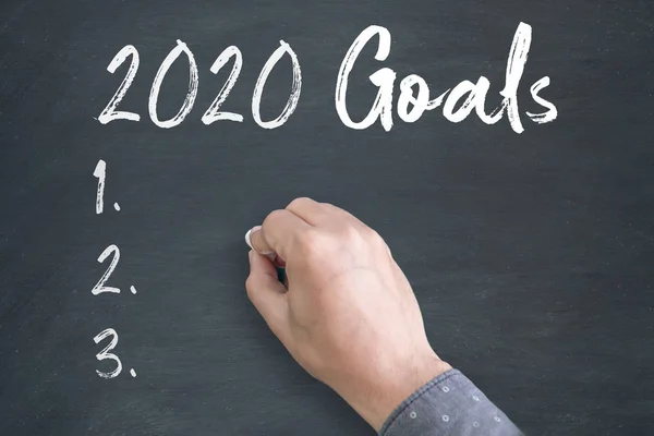 Young Man standing below blackboard with chalk drawing of new year 2020 Goals — 스톡 사진