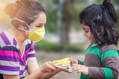Covid-19 Coronavirus ve Hava kirliliği pm2.5 konsepti. Korunmak ve Corona virüsünü durdurmak için kalabalık bir yerde maske takan küçük Hintli kız ve anne.