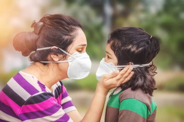 Covid-19 Coronavirus ve Hava kirliliği pm2.5 konsepti. Korunmak ve Corona virüsünü durdurmak için kalabalık bir yerde maske takan küçük Hintli kız ve anne.