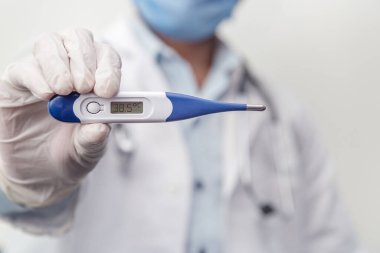 Steteskop kullanan doktor vücut ısısını, virüsten korunmayı, grip ve solunum hastalıklarını ölçmek için dijital termometre tutuyor. Coronavirus (COVID-19) salgını.