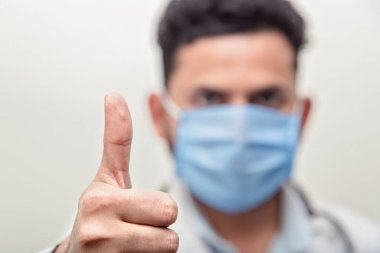 Beyaz önlüklü doktor, beyaz eldivenli ve beyaz arka planda tekstil tıbbi maskeli doktor. Diğer elinde ise korona virüslerine ve bakterilere karşı koruyucu aksesuarlar var.