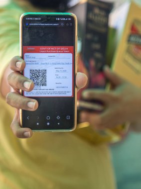Yeni Delhi, Hindistan - 16 Mayıs 2020: Akıllı telefon ekranındaki e-sembol resmi. Kalabalığı azaltmak için Delhi valisi likör satışı için e-jeton dağıtıyor. Bir müşteri, Covid-19 kilidinin ortasındaki bir dükkandan likör aldıktan sonra cep telefonundaki e-jetonu ayakkabıya bağlıyor.
