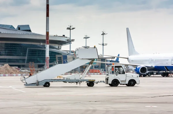 The tractor pulls the passenger boarding stairs at the airport apron beside to the terminal