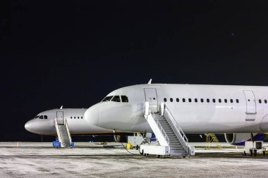 The front part of the two aircraft with passenger boarding stairs at night winter airport apron clipart