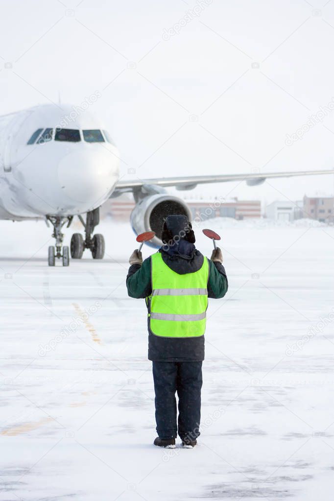 Airport marshaller meets the aircraft that parking in a cold winter weather