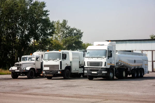 Three white tank truck aircraft refuelers in the parking lot near the garages