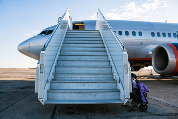 Airplane with a passenger boarding steps on the airport apron with a stroller prepared for the carriage of children