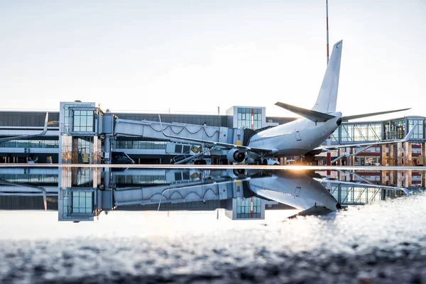 Passenger airplane parked to a air bridge with reflection in a puddle