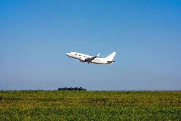 Green field, blue sky and white passenger plane takes off
