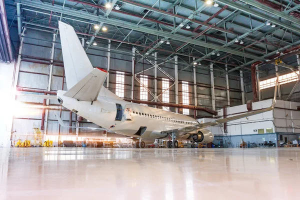 Sabah ışığında beyaz yolcu uçağı hangarda. Uçuş işlemleri için mekanik sistemleri kontrol ediyorum. Uçak bakım altında.