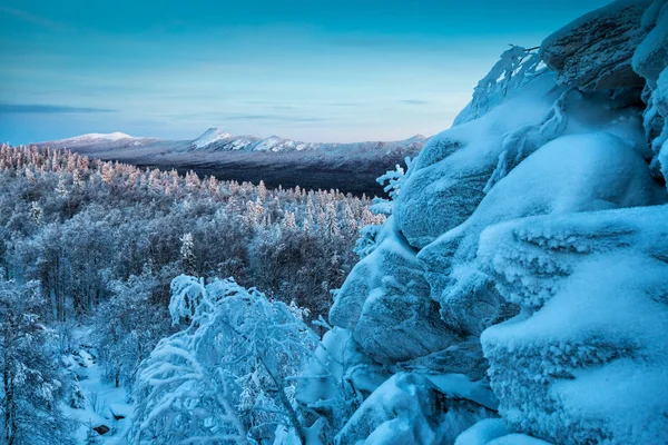 Rock, snow capped mountains and winter forest in the evening light
