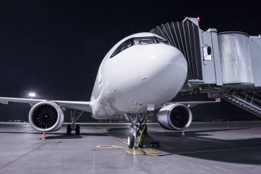 Beyaz bir yolcu uçağı, havaalanı önlüğündeki dış güç kaynağına bağlı olarak jetway 'de duruyor.