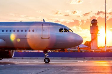 Bir yolcu uçağının ön tarafına yakın çekim. Hava alanının önlüğünde taksicilik yapan hava araçları gün doğumunun ışıltıları altında.
