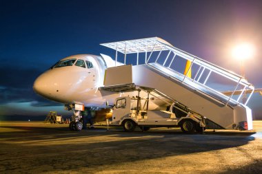 Gece havaalanı önlüğündeki merdivenlerde beyaz yolcu uçağı.