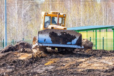 Sarı buldozer inşaat alanında zemini dümdüz ediyor.