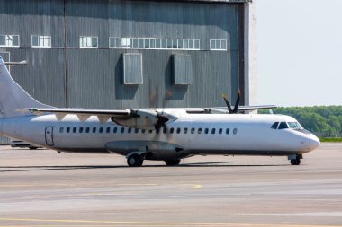 Havaalanı önlüğündeki hangara beyaz yolcu turbo pervanesi taksisi.