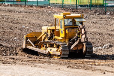 Sarı buldozer inşaat alanında zemini dümdüz ediyor.