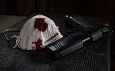 Siyah masa kanlı bir tıbbi maske ve silahla