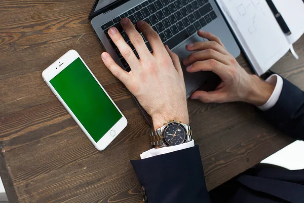 Bilgisayarı, tableti ve telefonu olan bir ofis masası. Adamın elleri yeşil ekranlı bir akıllı telefonu tutuyor. Ofis İşçi Masası