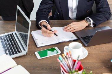 Bilgisayarı, tableti ve telefonu olan bir ofis masası. Erkek eli kalem tutar. Ofis İşçi Masası