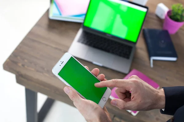 Bilgisayarı, tableti ve telefonu olan bir ofis masası. Adamın elleri yeşil ekranlı bir akıllı telefonu tutuyor. Ofis İşçi Masası