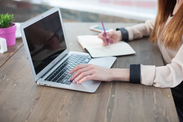Bilgisayarlı, tabletli bir ofis masası. Kadın ellerinde fuşya renkli bir kalem. Yazmak için sarı çarşaflar, kalemler ve masanın üstündeki saksıda bir çiçek.