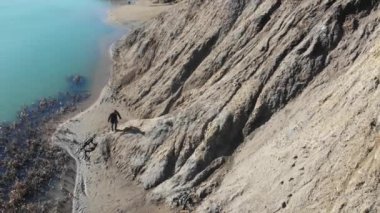 Köpeği olan bir adam, mavi bir göl boyunca yürür.