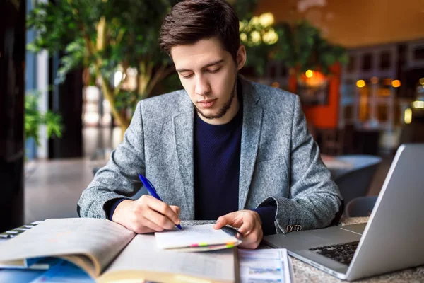 Tiro de jovem estudante do sexo masculino sentado à mesa e escrevendo no caderno . — Fotografia de Stock