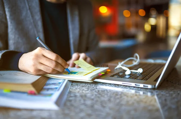 Tiro de jovem estudante do sexo masculino sentado à mesa e escrevendo no caderno . — Fotografia de Stock