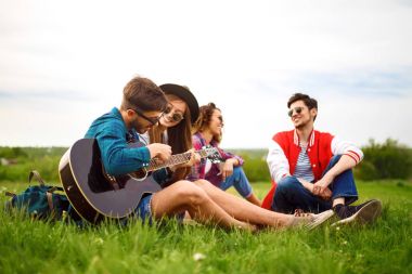 Grup arkadaşıyla birlikte eğleniyor. Adam gitar çalıyor. Herkes büyük bir ruh var.