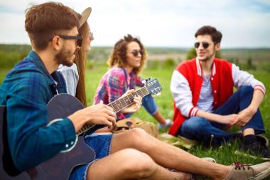Grup arkadaşıyla birlikte eğleniyor. Adam gitar çalıyor. Herkes büyük bir ruh var.