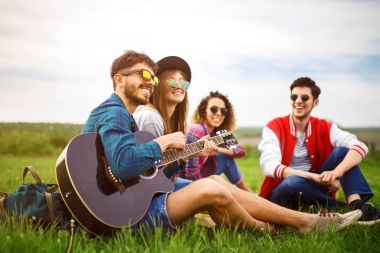 Grup arkadaşıyla birlikte eğleniyor. Adam gitar çalıyor. Herkes büyük bir ruh var.
