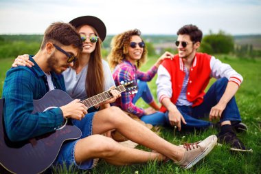 Grup arkadaşıyla birlikte eğleniyor. Adam gitar çalıyor. Herkes büyük bir ruh var.