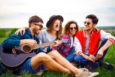 Grup arkadaşıyla birlikte eğleniyor. Adam gitar çalıyor. Herkes büyük bir ruh var.