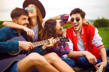 Grup arkadaşıyla birlikte eğleniyor. Adam gitar çalıyor. Herkes büyük bir ruh var.