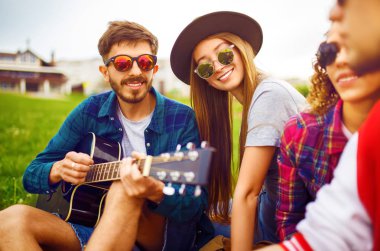 Grup arkadaşıyla birlikte eğleniyor. Adam gitar çalıyor. Herkes büyük bir ruh var.