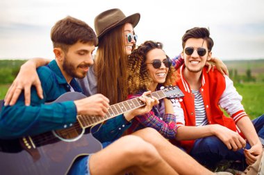 Grup arkadaşıyla birlikte eğleniyor. Adam gitar çalıyor. Herkes büyük bir ruh var.