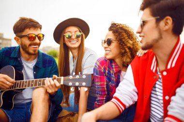 Grup arkadaşıyla birlikte eğleniyor. Adam gitar çalıyor. Herkes büyük bir ruh var.