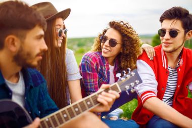 Grup arkadaşıyla birlikte eğleniyor. Adam gitar çalıyor. Herkes büyük bir ruh var.